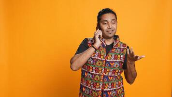 Man discussing with best friend over telephone call, enjoying leisure time. Upbeat person wearing indian attire talking with mate in phone call, isolated over studio backdrop, camera B photo