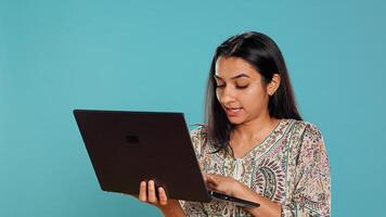 Woman composing email, carefully typing on laptop keyboard, struggling to think of what to write. Indian person sending mail online, brainstorming message idea, studio background, camera B photo