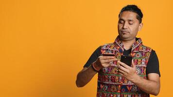 Indian man adding payment method on mobile phone website, purchasing stuff, isolated over studio background. Client does internet shopping, typing debit card info on cellphone, camera A photo