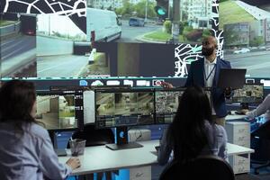 Middle eastern team leader gives instructions to his staff in control center, pointing at satellite map and CCTV footage to guide delivery trucks on their way to the order shipment destination. photo