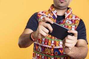Close up of player playing videogames on smartphone, enjoying relaxation, yellow studio backdrop. Focus on phone used by person in blurry background to do gaming, competing against other players photo