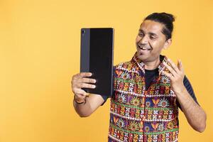 Joyous man having positive mood using tablet to take selfies from all angles. Radiant person taking photos using device selfie camera, feeling stoked, isolated over studio backdrop