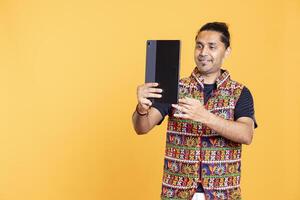 Cheerful indian man grinning, using tablet to take selfies from all angles. Upbeat social media user taking pictures using device selfie camera, feeling excited, studio background photo