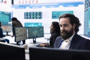 CEO reviewing business activity numbers on annual reports in control room, examining progress status and infographics. Finance advisor looks into big data analytics online at pc. photo