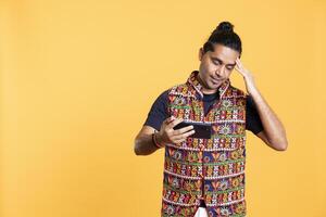 Gamer annoyed after losing online multiplayer videogame, being defeated by rival players. Indian man shocked and gutted after seeing game over message, holding phone, studio background photo