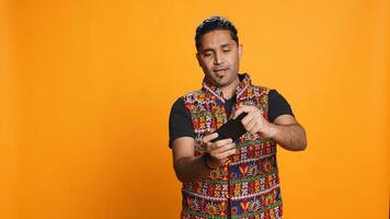 Cheerful Indian person in traditional clothing entertained by videogames on smartphone. Joyous player enjoying game on phone, having fun online, studio backdrop, camera B photo