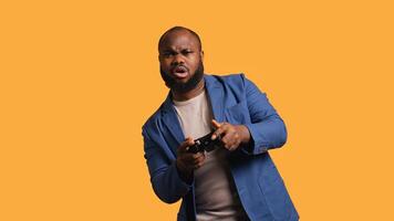Portrait of cheerful BIPOC man playing videogames holding controller, studio background. Gamer smiling, having fun by participating in PvP online multiplayer game using console system, camera B photo
