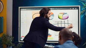 Financial analyst briefing his team about new company objectives, making budget and sales presentation with interactive board. Specialist addressing resource allocation and project planning. Camera A. photo