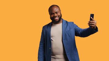 African american narcissistic man using cellphone to take selfies from all angles. Vain social media user taking photos using phone selfie camera, smiling happily, studio background, camera B