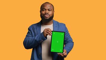 Portrait of african american man doing influencer marketing using green screen tablet, studio background. Smiling BIPOC person holding empty copy space mockup device, camera A photo