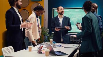 Happy confident coworkers meeting in a conference room to review their results, studying infographics and feedback from stakeholders. Pleased team leader and employees share impressions. Camera B. photo