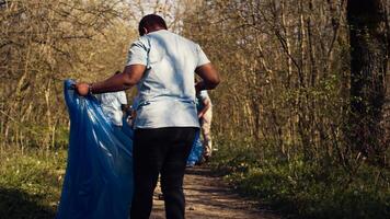 Diverse activists group using claw tools to grab trash and plastic, storing it in garbage disposal bags. People gathering to collect rubbish and recycling for sustainable lifestyle. Camera B. photo