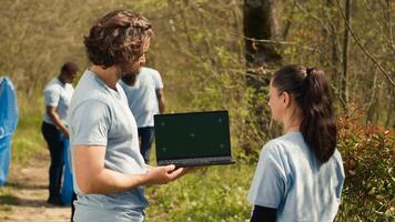 Team of climate and nature activists using laptop with greenscreen near a forest, volunteering to pick up trash and plant trees for future generations. Environmental protection. Camera A. photo
