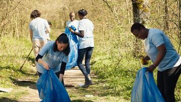 Group of diverse volunteers collecting rubbish from the woods and recycling in a garbage disposal bag, litter cleanup responsibility. Ecology activists picking up trash and plastic waste. Camera A. photo