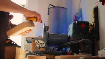Woodworking specialist using manual sandpaper to sander lumber block, making furniture in assembling shop during job shift. Handyman polishing surface of piece of wood with abrasive material, camera B photo