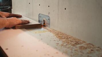 Carpenter in studio puts wood block through spindle moulder, creating smooth edges on wooden pieces. Cabinetmaker in joinery using heavy machinery to craft joints for furniture, camera B close up photo