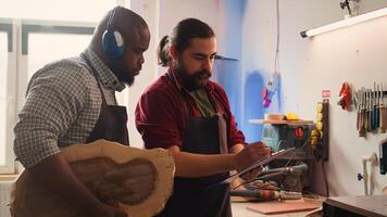 Carpenter and colleague looking over technical schematics, brainstorming ideas for wooden object. Master and apprentice analyzing blueprints to execute furniture assembling project, camera B photo