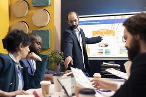 Chairman of the board reviews business expansion plans, team supervisor and the members look into data visualizations statistics. Corporate associates seek to boost sales and earnings. photo