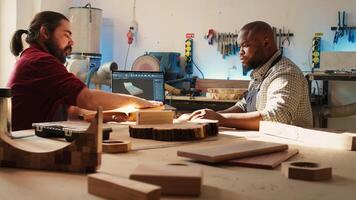 Artisan and apprentice comparing wood art piece with schematic displayed on CAD software on laptop. Woodworking experts in studio crosschecking wooden object with notebook blueprint, camera B photo