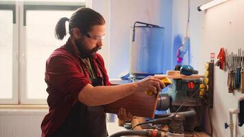 Artisan with safety glasses next to apprentice using sanding block to remove imperfections on wood. Creative man wearing protective gear enjoying diy hobby, using sandpaper to do sanding, camera B photo