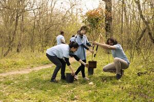 Volunteers and a child planting a tree and covering hole in the ground, contributing to reforestation and growing vegetation in the woods. Motivated people working together for the planet. photo