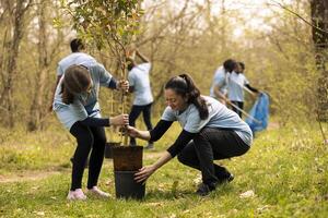 mamá y su pequeño niña tomando un árbol fuera de el maceta y planta él, haciendo voluntario trabajo a ayuda con repoblación forestal y ambiental proteccion. activistas tomando acción a ayuda natural hábitat. foto