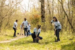 Diverse activists joining forces in digging holes to plant trees with devotion to reforestation concept, nurturing its growth and preserving the seedlings. Focused group of environmentalists. photo