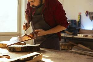 Craftsperson in carpentry shop starting restoration project on wood block, applying lacquer on surface. Carpenter coloring plank with paintbrush, doing handwork in studio photo