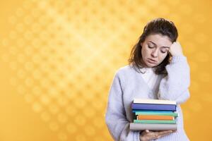 Portrait of upset woman holding pile of books, conveying hate of reading concept, isolated over studio background. Annoyed person with stack of novels showing disregard for literature photo