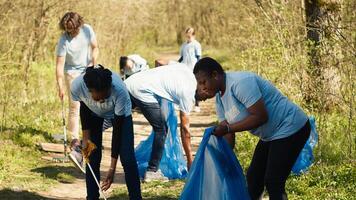 Environmental activists collecting rubbish and plastic waste in garbage bag, using littler cleanup tools to pick up trash from the forest. Women doing voluntary work to protect ecosystem. Camera A. photo
