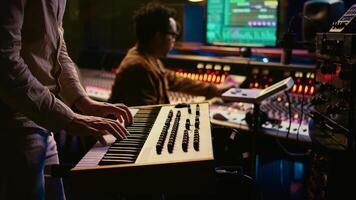 Musician playing piano midi controller in control room at professional recording studio, creating sounds with electronic keyboard notes. Sound engineer does mix and master on files. Camera B. photo
