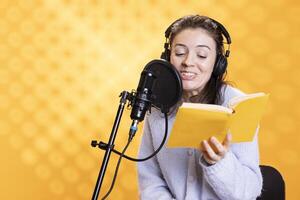 Jolly narrator wearing headset reading aloud from book into mic against yellow background. Upbeat professional voice actor recording audiobook, creating engaging media content for listeners photo