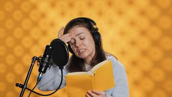 Woman feeling tired while doing voiceover of book and producing audiobook all day. Narrator suffering headache from fatigue, doing digital recording of novel, isolated over studio background, camera A photo