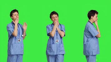 Medical assistant feeling extremely sleepy against greenscreen backdrop, being overworked after the night shift. Woman nurse yawns and feels exhausted in studio, burnout and anxiety. Camera B. photo