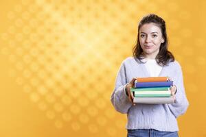 Portrait of happy woman holding pile of books, enjoying reading hobby for relaxation purposes. Upbeat bookaholic person with stack of novels in arms enjoying leisure time, studio background photo