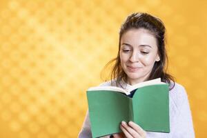 Happy woman browsing through funny book pages, grinning, having fun, isolated over studio background. Joyful person smiling while reading comical novel, enjoying leisure time photo