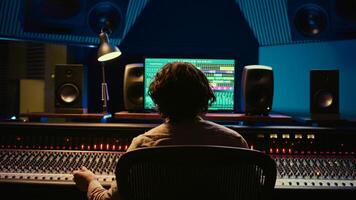 Joyful pleased music producer enjoying his high quality track in control room, finishing project with knobs and sliders. Audio engineer mixing sounds in post production. Camera B. photo