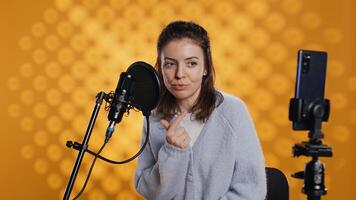 Narrator looking at phone camera, filming herself reading book for kids, creating audiobook, studio background. Content creator doing vlog while producing digital recording of children novel, camera B photo