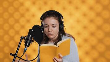 Woman does voiceover reading of book to produce audiobook using dramatic acting. Narrator uses storytelling skills and expressive sounds while producing recording of novel, studio background, camera A photo