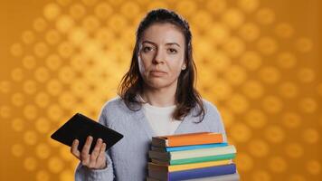 Woman debating between physical books and ebooks on ereader, isolated over studio background. Bookworm comparing paper novels and digital literature on tablet, technology concept, camera B photo