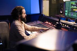 Control room audio engineer processing and mixing sounds with sliders and knobs, working on music post production in professional studio. Technician producing tracks on electronic console. photo