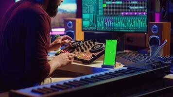 Sound engineer working on mixing and mastering techniques in his home studio, using phone with greenscreen display while he is recording audio. Artist operating soundboard and amplifier. Camera A. photo