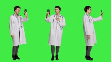 Medic specialist having remote videocall conversation with patients on smartphone internet connection, greenscreen backdrop. Doctor discusses about disease with people on videoconference. Camera A. photo
