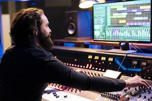 Audio technician operating daw software for mixing and mastering tunes in studio, editing music on control panel board. Skilled producer composing records with faders and switchers. photo