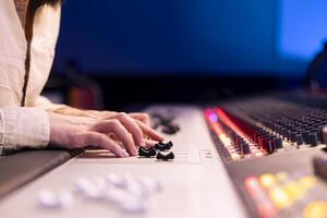 Music producer pushing faders and sliders on control panel board in studio, adjusting volume levels on songs and removing white noise. Sound engineer operates technical equipment. Close up. photo
