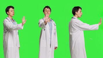 Woman physician raising palm and doing stop sign in studio, expressing rejection and denial against greenscreen backdrop. General practitioner showing warning symbol with negative reaction. Camera B. photo