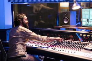 Music engineer applying mix and master techniques on old recordings, pressing buttons and switchers to add audio effects in post production. Record producer creating new songs with console. photo