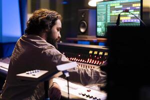 Audio technician working on recording and editing new music in studio, processing sounds by using mixing console and twisting knobs in control room. Sound producer pushing buttons and sliders. photo