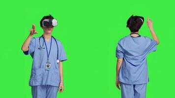 Health specialist using vr headset to examine patient diagnosis, stands against greenscreen backdrop. Nurse works with artificial intelligence virtual reality glasses, three dimensional. Camera B. photo