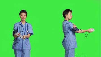 Medical assistant showing tonometer used to measure arterial blood pressure, standing against greenscreen backdrop. Nurse working with sphygmomanometer tool to take measurement at checkup. Camera B. photo